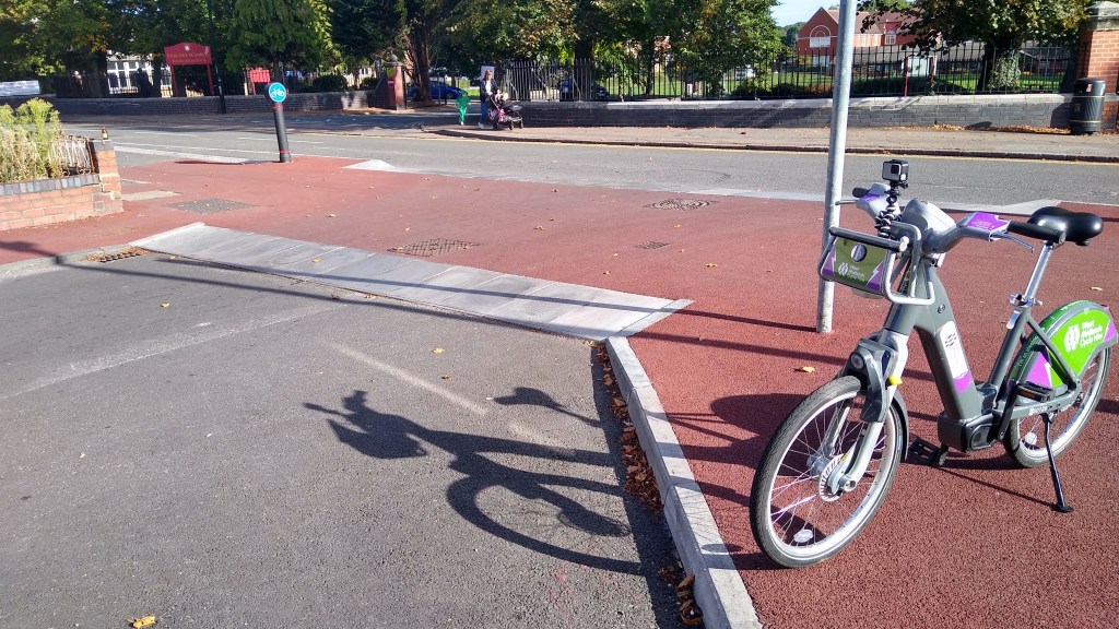 A view of the junction from the side street where the ramped kerbs units can be aseen. A bike is parked to the right.