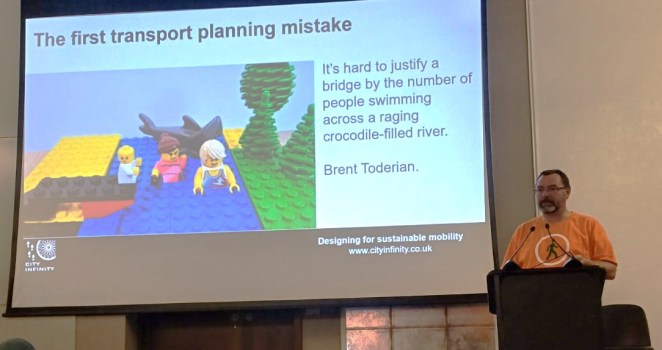 A presentation slide featuring a Lego scene illustrating a quote by Brent Toderian what says "it's hard to justify a bridge by the number of people swimming across a crocodile-filled river".