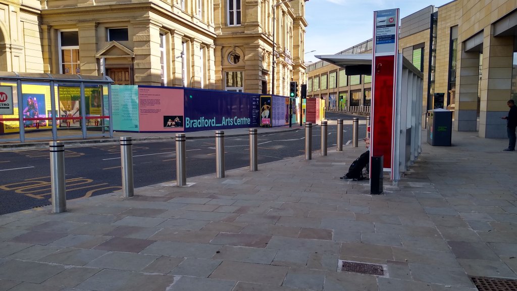 The view along a bus stop from away and just beyond the shelter with a line of fat bollards along the boarding zone.
The view along a bus stop from away and just beyond the shelter with a line of fat bollard along the boarding zone.